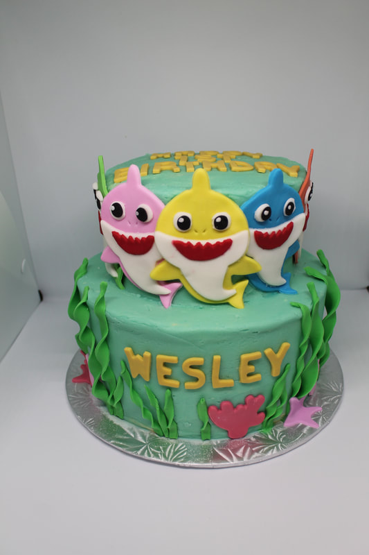 Under the sea cake with three sharks, one pink, one yellow, and one blue