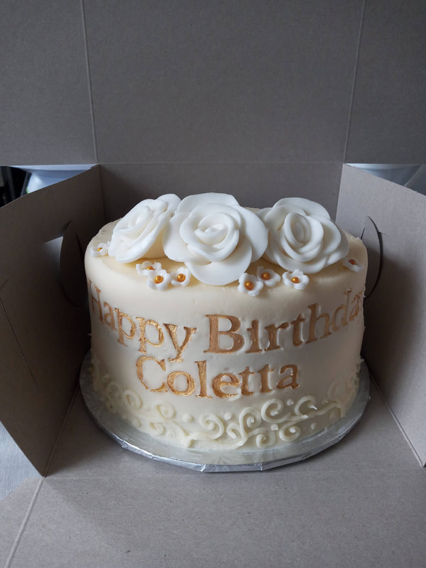 White birthday cake with white flowers and gold lettering