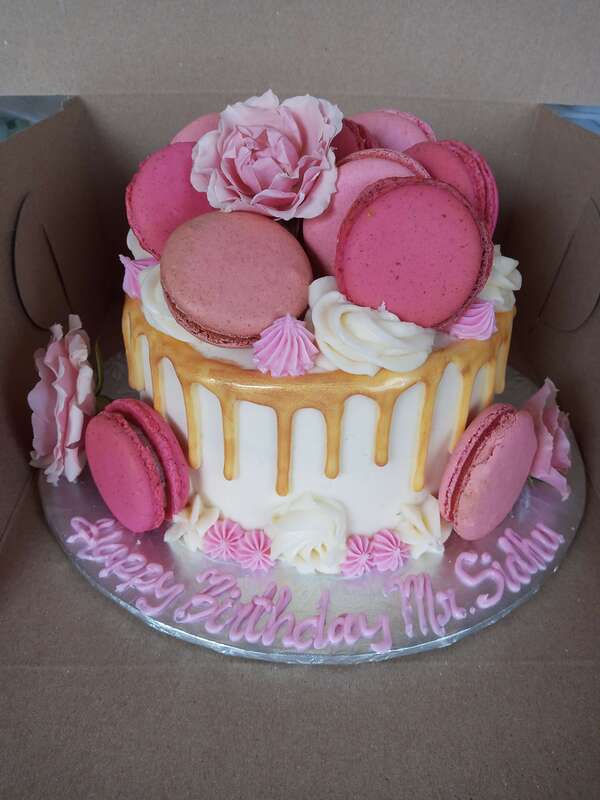 White cake with gold drip icing and pink macarons