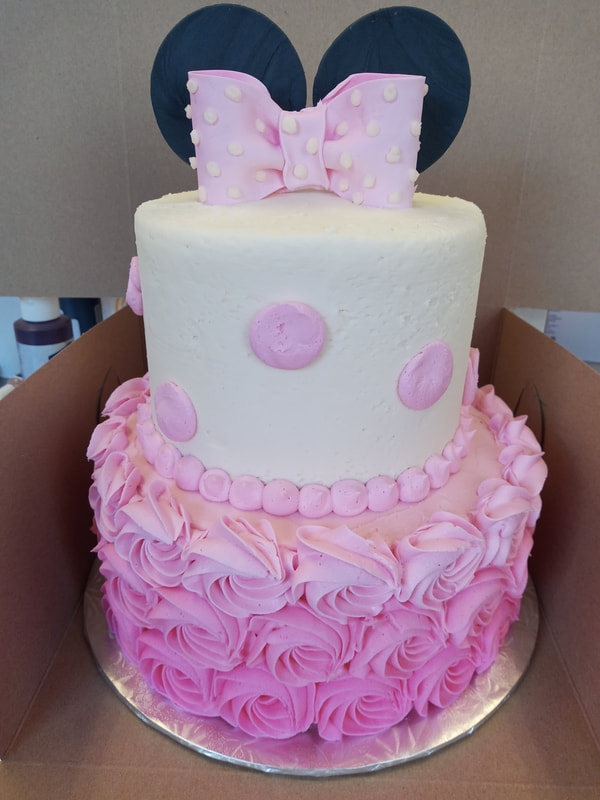 White two tiered cake with pink rosettes on the bottom tier, pink polka dots on the top tier and a pink bow on the top