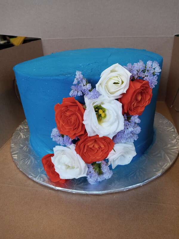 Blue cake with red, white and purple flowers on the side