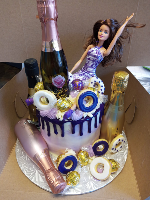 White cake with blue and gold decorations and a Barbie and bottles of alcohol