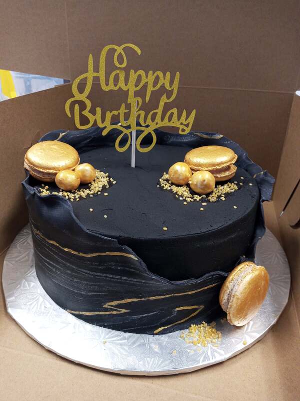 Black cake with a black and gold marble wrap and gold macarons and decorations