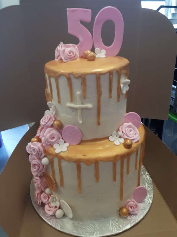 Two tiered whit cake with gold drip icing and white pink and gold decorations